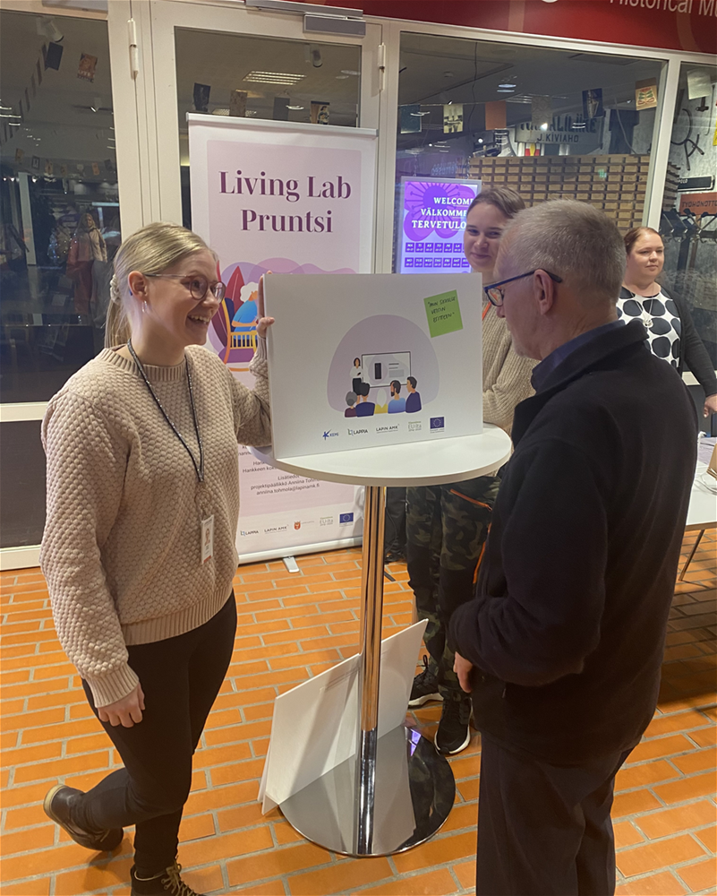 Marjo Jussila ja vanhempi mieshenkilö tutkivat havainnekuvaa pystypöydän ympärillä seisten.
