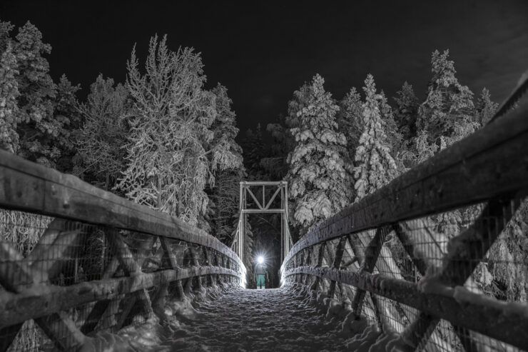 Henkilö otsalampun valossa talvisen ja pimeän sillan päässä.