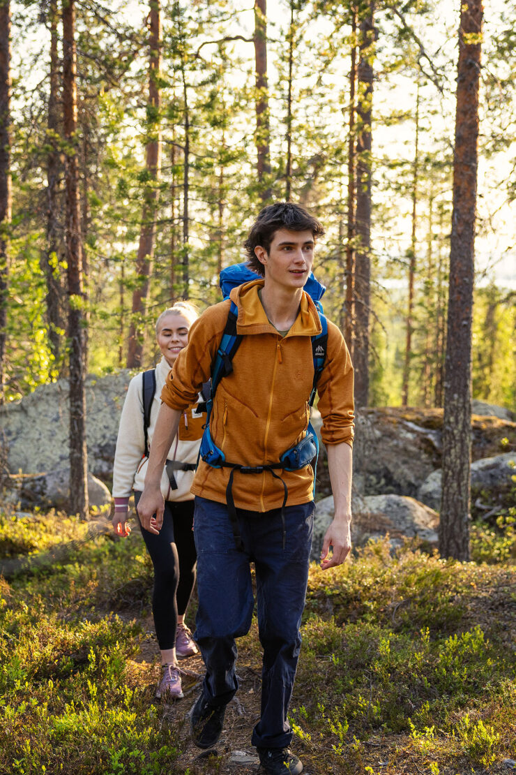 Nuori mies ja nainen kävelevät peräkkäin polulla. Ympärillä näkyy mäntymetsää ja kivikkoa. Henkilöillä on reput selässä.