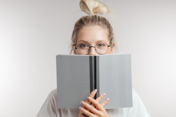 A woman peeks from behind a book.