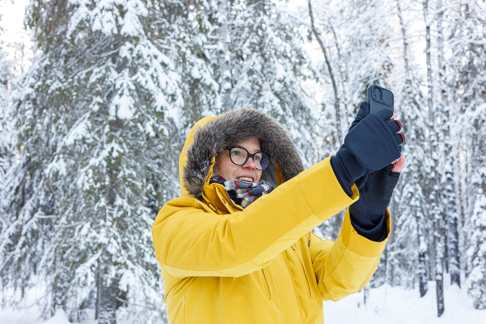 Nainen ottaa selfien lumisessa metsässä.