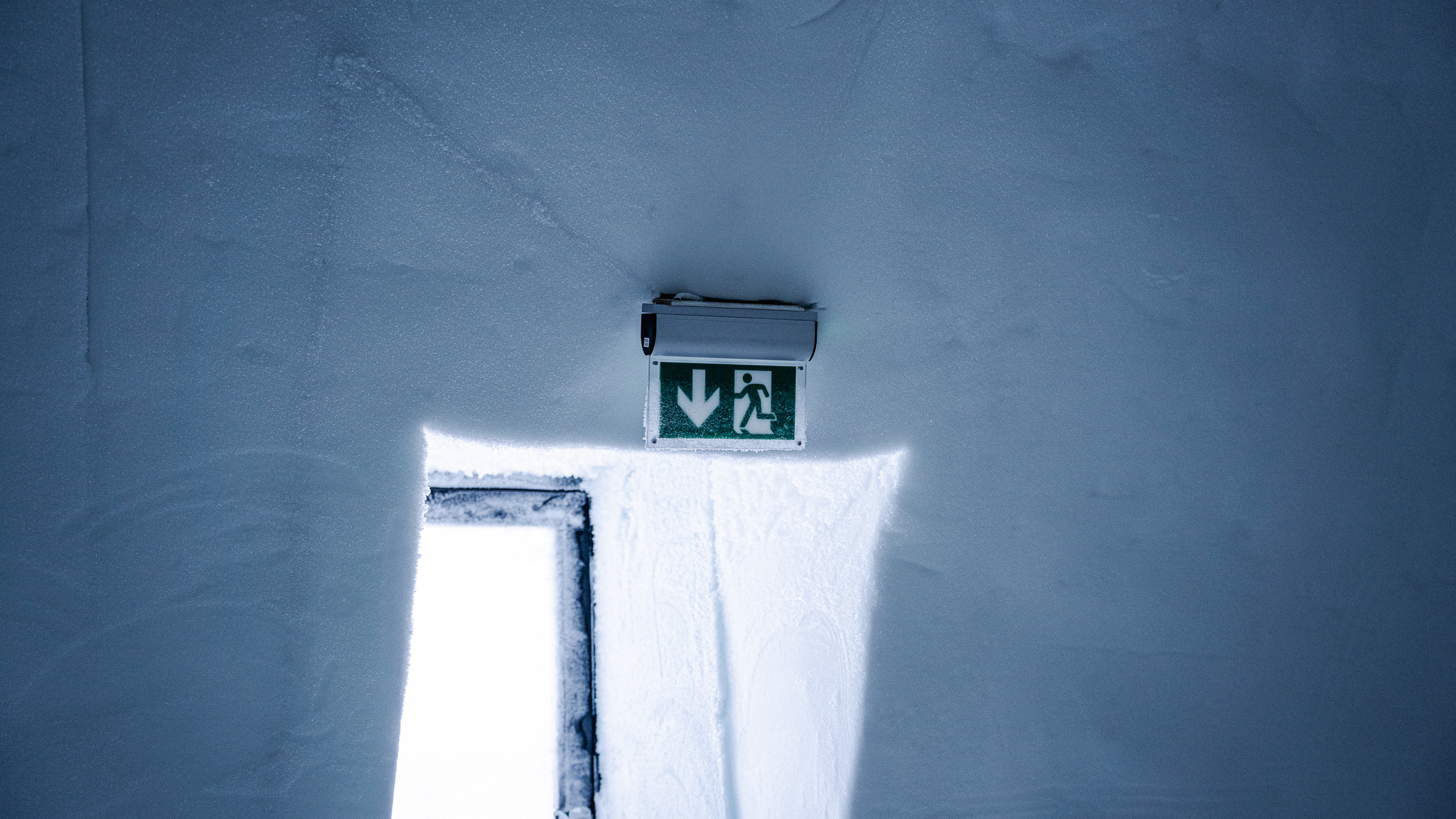 Valaistu hätäpoistumistien opaste lumirakenteeseen tehdyn oviaukon yläpuolella. 