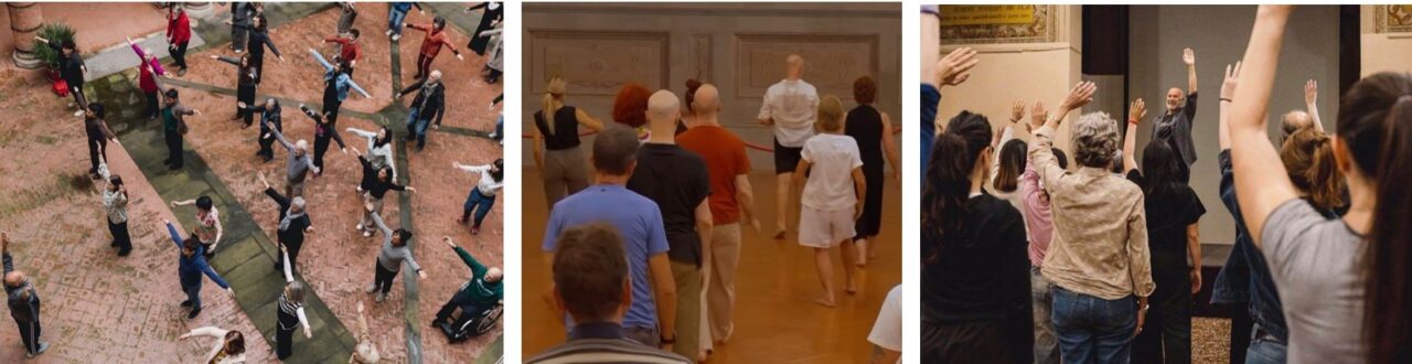 Figure 12. A photograph shows a group of people standing in an open space, viewed from a slightly elevated angle. One person stands at the front demonstrating a movement, while others follow with their arms extended out to the sides, including one participant using a wheelchair. Figure 13. A photograph shows a group of people standing barefoot in a large indoor space with decorative walls and wooden flooring. The group is viewed from behind, following a person at the front who demonstrates a movement, as the others walk forward together in a guided activity. Figure 14. A photograph shows a group of people standing in a hall facing a person at the front who raises an arm. The participants mirror the movement by lifting their hands in a guided group activity.