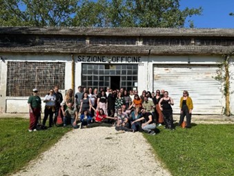 Image Description – A large group of people all gathered in front of a building on a sunny day. They all wearing different colours and posing for the camera.