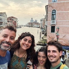 A group of friends all huddled together. They are all smiling at the camera. You can see Venice behind them.