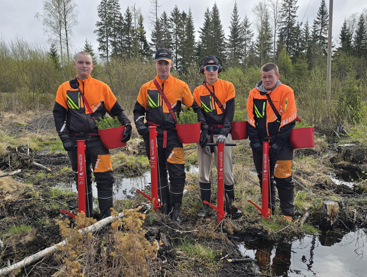 Neljä nuorta henkilöä metsurin tarvikkeissa metsän reunalla.