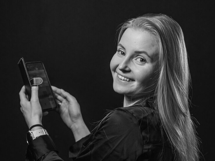 Henkilö kannattelee kaksin käsin matkapuhelinta edessään ja hymyilee olan yli kameralle.