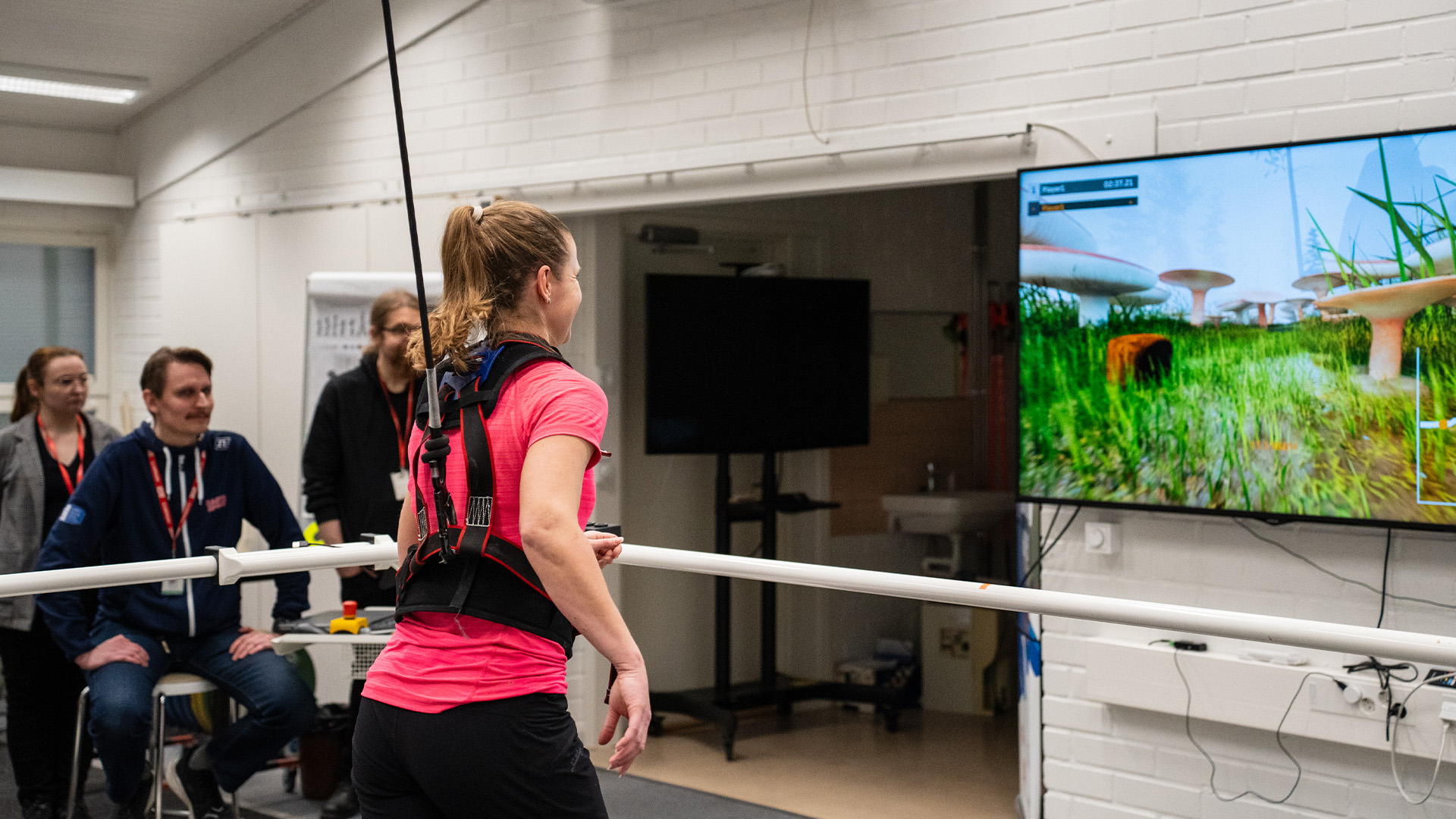 Henkilö juoksee Rodby-juoksumatolla turvavaljaisiin kytkettynä, edessä näkyy televisiossa pelin fantasiakenttä, ihmisiä valvoo ja seuraa juoksua 