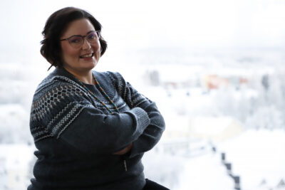 Henkilö katsoo kameraan hymyillen, kädet puuskassa.