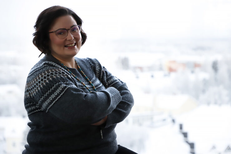 Henkilö katsoo kameraan hymyillen, kädet puuskassa.